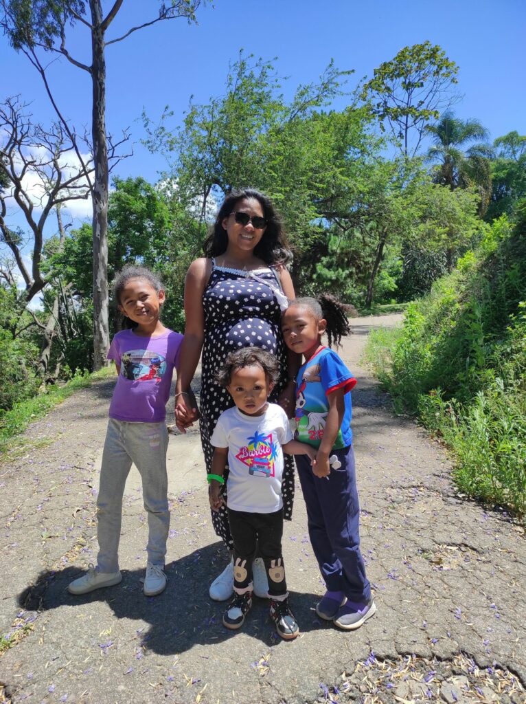 Une femme enceinte se promenant dans le parc avec ses trois enfants, souriante et rayonnante de bonheur. 